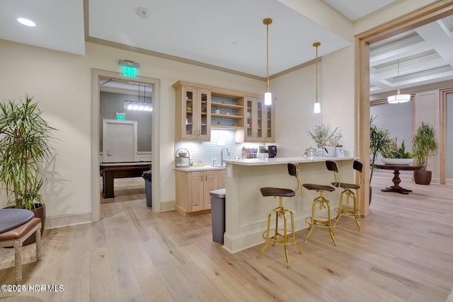 kitchen featuring light wood finished floors, glass insert cabinets, a breakfast bar, light countertops, and a sink