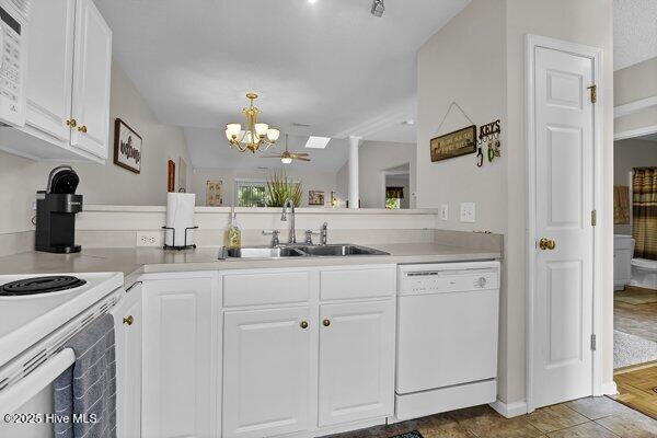 kitchen with sink, white appliances, hanging light fixtures, a notable chandelier, and white cabinets