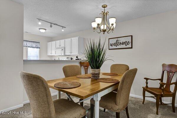 carpeted dining space featuring an inviting chandelier, rail lighting, and a textured ceiling