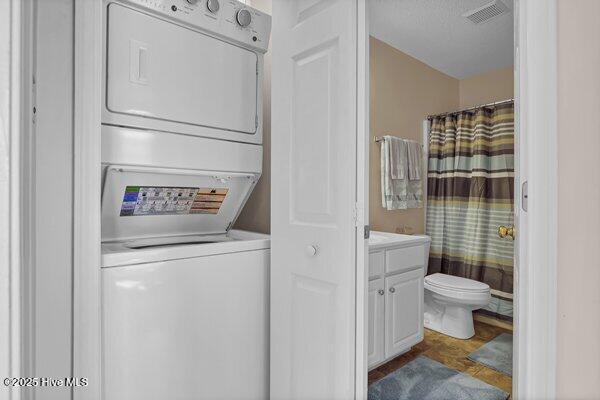 washroom featuring a textured ceiling and stacked washer / dryer