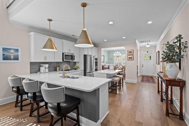 kitchen featuring a breakfast bar, white cabinetry, stainless steel appliances, decorative light fixtures, and kitchen peninsula