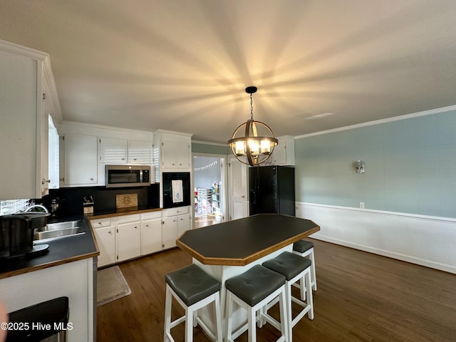 kitchen with sink, white cabinetry, ornamental molding, black fridge, and decorative light fixtures