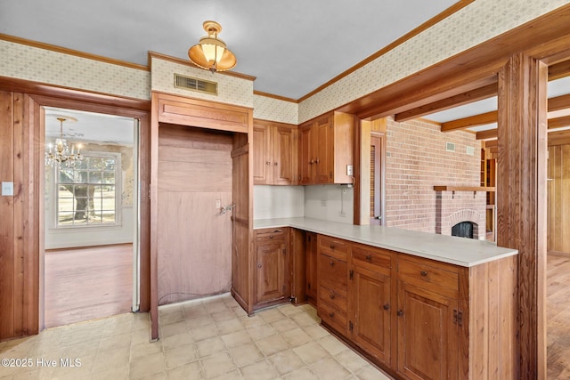 kitchen featuring a brick fireplace, a chandelier, decorative light fixtures, crown molding, and kitchen peninsula