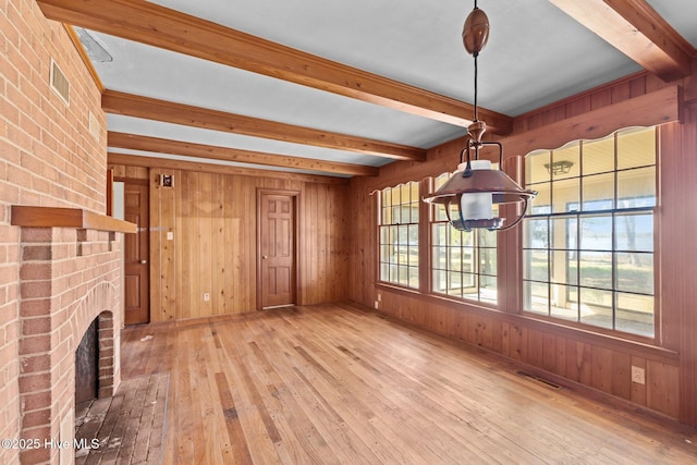 unfurnished living room featuring wood walls, beamed ceiling, wood-type flooring, and a wealth of natural light