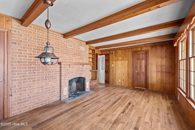 unfurnished living room with a brick fireplace, light wood-type flooring, beamed ceiling, and wood walls