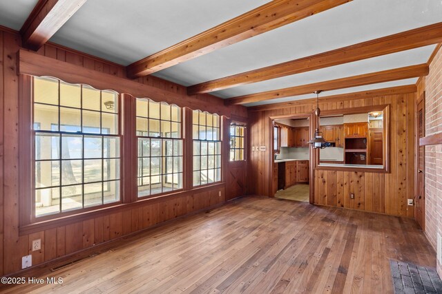 unfurnished living room featuring light hardwood / wood-style floors, beamed ceiling, and wooden walls