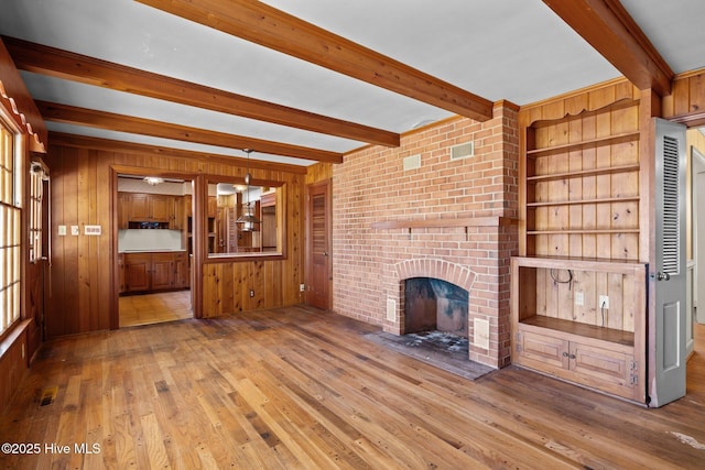 unfurnished living room featuring beam ceiling, light hardwood / wood-style flooring, wood walls, and a brick fireplace