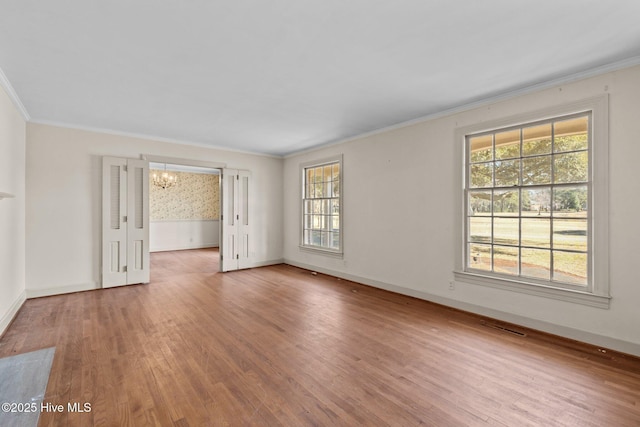 empty room with a notable chandelier, ornamental molding, wood-type flooring, and a healthy amount of sunlight