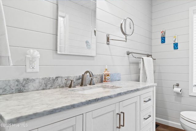 bathroom featuring toilet, wood walls, and vanity