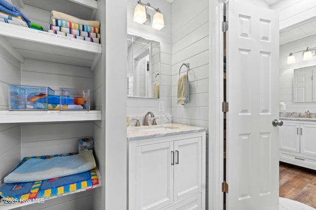 bathroom featuring a sink, wood walls, two vanities, and wood finished floors