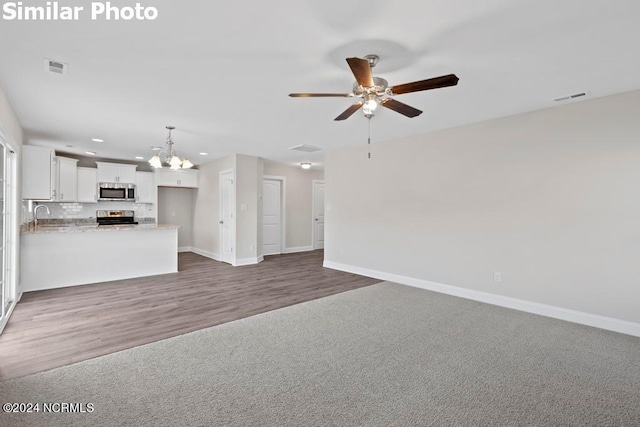 unfurnished living room featuring sink, dark carpet, and ceiling fan with notable chandelier