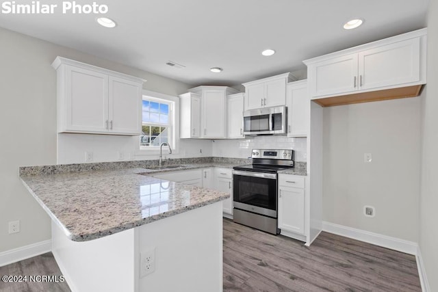 kitchen featuring white cabinetry, sink, hardwood / wood-style flooring, kitchen peninsula, and stainless steel appliances