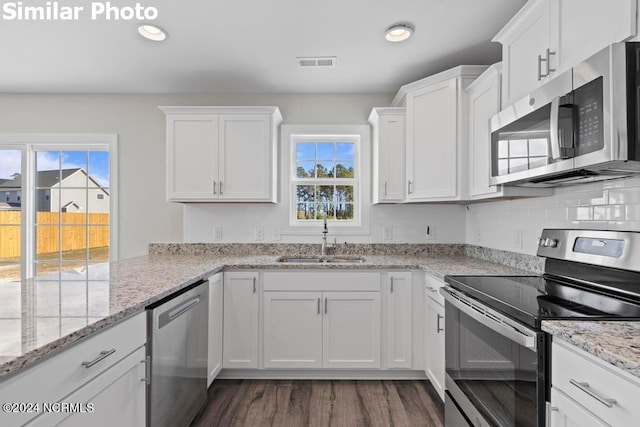 kitchen with white cabinetry, sink, light stone counters, stainless steel appliances, and dark wood-type flooring