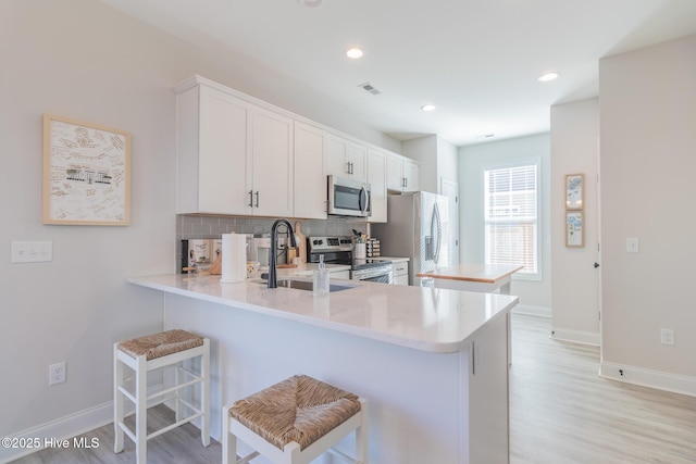 kitchen with sink, a breakfast bar area, appliances with stainless steel finishes, white cabinetry, and kitchen peninsula