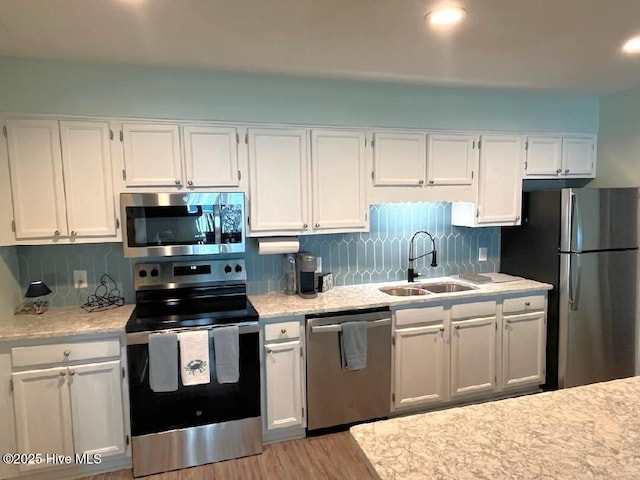 kitchen featuring white cabinetry, sink, backsplash, light hardwood / wood-style floors, and stainless steel appliances