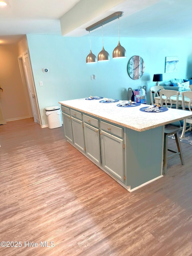 kitchen featuring pendant lighting, a kitchen island with sink, gray cabinetry, and light hardwood / wood-style floors