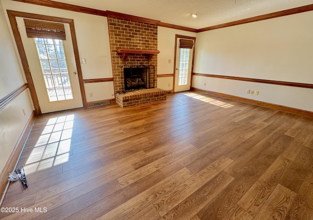 unfurnished living room featuring crown molding, a brick fireplace, hardwood / wood-style floors, and a textured ceiling