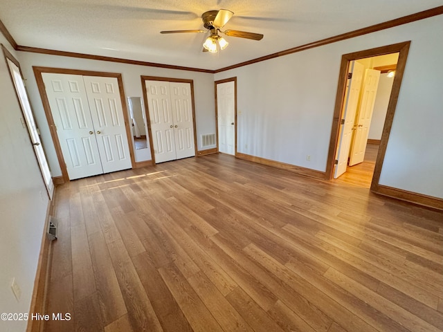 unfurnished bedroom featuring crown molding, ceiling fan, multiple closets, and light hardwood / wood-style flooring