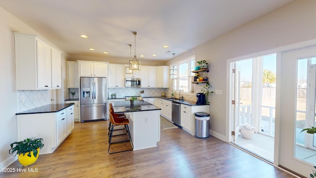 kitchen featuring a kitchen bar, appliances with stainless steel finishes, a kitchen island, pendant lighting, and white cabinets