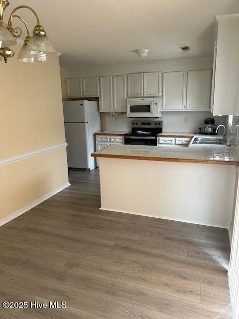 kitchen with white appliances, dark wood-type flooring, decorative light fixtures, and kitchen peninsula