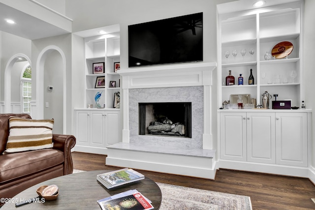 living room with built in shelves, a high end fireplace, and dark hardwood / wood-style flooring