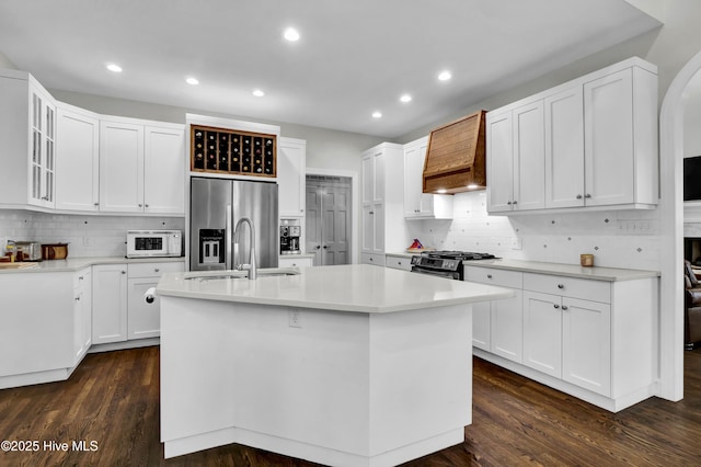 kitchen featuring an island with sink, custom range hood, and white cabinets