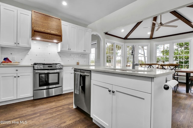 kitchen with stainless steel appliances, a kitchen island, vaulted ceiling with beams, and white cabinets