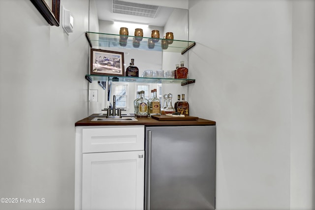 bar featuring sink, white cabinets, and stainless steel refrigerator