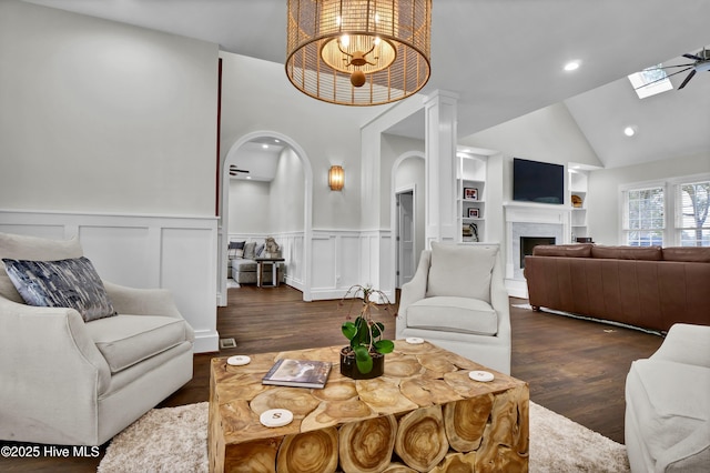 living room with built in shelves, lofted ceiling with skylight, and dark hardwood / wood-style floors