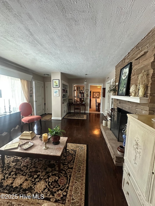 living room with a stone fireplace, dark hardwood / wood-style floors, and a textured ceiling