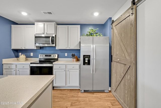 kitchen featuring a barn door, appliances with stainless steel finishes, white cabinets, and light hardwood / wood-style flooring