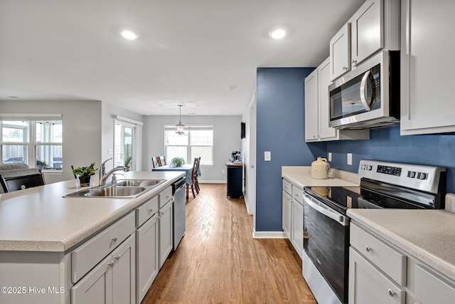 kitchen with decorative light fixtures, an island with sink, white cabinetry, sink, and stainless steel appliances