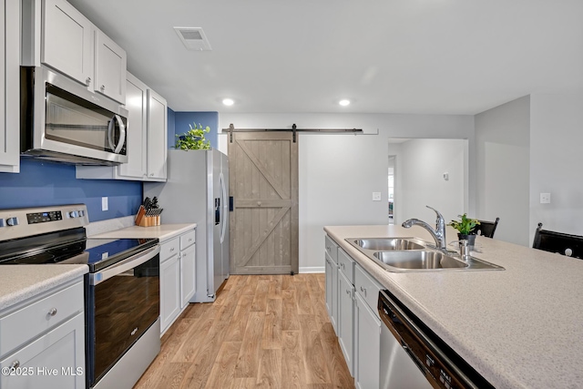 kitchen featuring appliances with stainless steel finishes, sink, white cabinets, a barn door, and light wood-type flooring