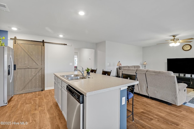 kitchen featuring sink, a kitchen island with sink, white cabinetry, stainless steel appliances, and a barn door