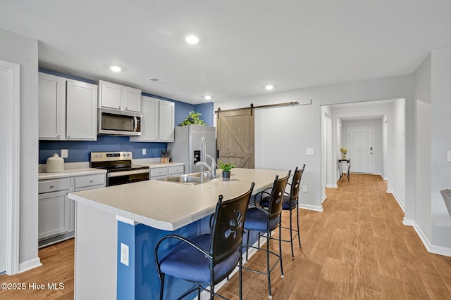 kitchen featuring appliances with stainless steel finishes, sink, a breakfast bar area, a kitchen island with sink, and a barn door