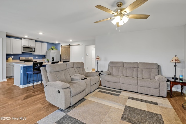 living room with ceiling fan, a barn door, and light hardwood / wood-style flooring