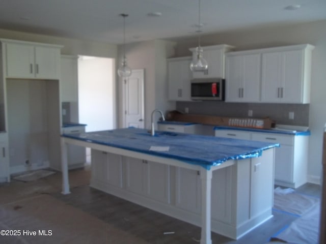 kitchen with stainless steel microwave, white cabinets, a center island with sink, and a sink