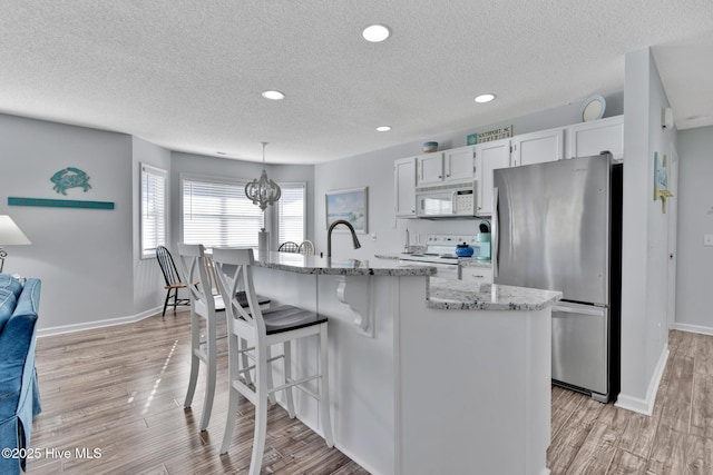 kitchen featuring white appliances, white cabinetry, an island with sink, decorative light fixtures, and light wood-type flooring