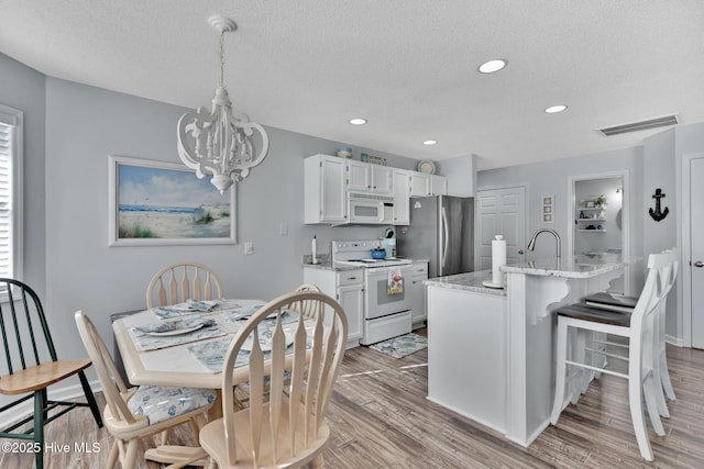 kitchen featuring white appliances, white cabinetry, light stone counters, light hardwood / wood-style floors, and an island with sink