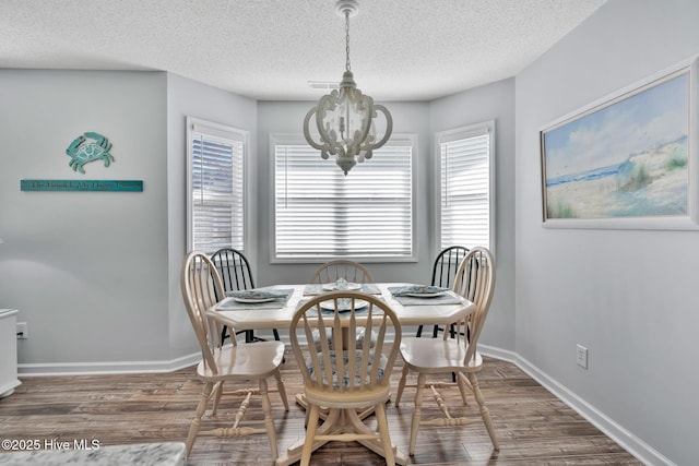 dining area with an inviting chandelier, dark hardwood / wood-style floors, and a textured ceiling