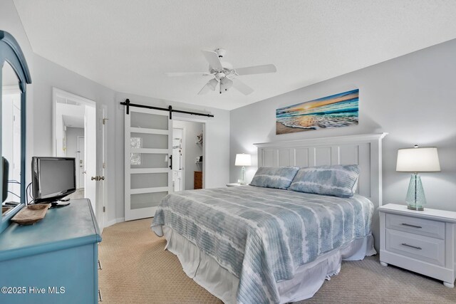 bedroom with a textured ceiling, light colored carpet, a barn door, and ceiling fan