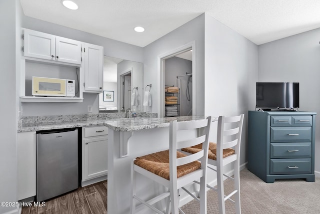 kitchen with light stone countertops, a breakfast bar area, white cabinets, and stainless steel refrigerator