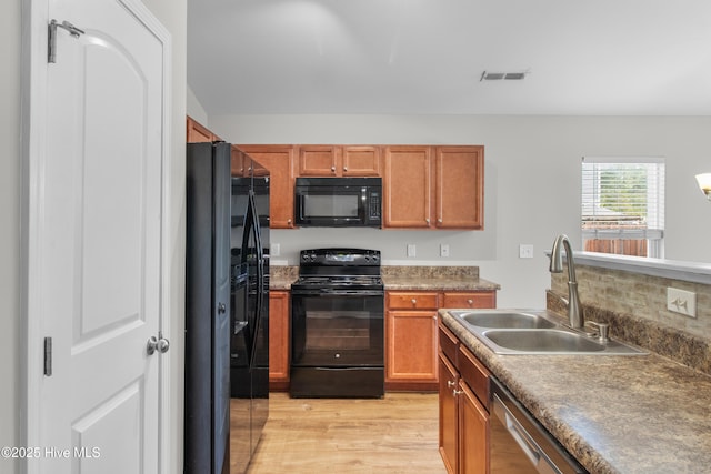 kitchen featuring a sink, black appliances, light wood-style floors, and brown cabinets