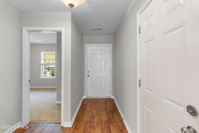 corridor with dark wood-type flooring, visible vents, and baseboards