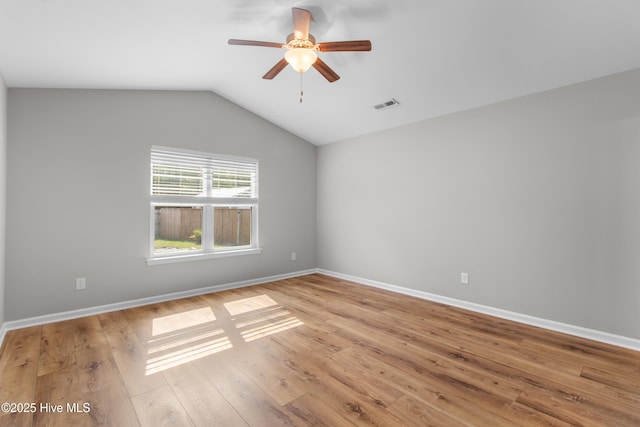 spare room featuring baseboards, vaulted ceiling, light wood-style flooring, visible vents, and ceiling fan