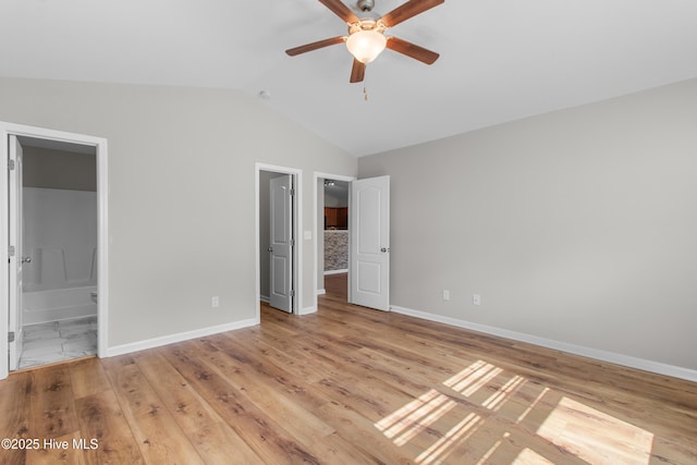 unfurnished bedroom featuring ensuite bathroom, baseboards, light wood-style floors, and vaulted ceiling