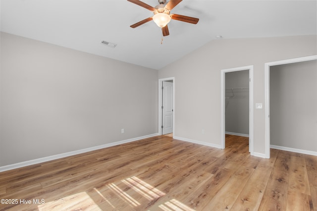 unfurnished bedroom featuring a closet, a spacious closet, light wood-style flooring, visible vents, and lofted ceiling