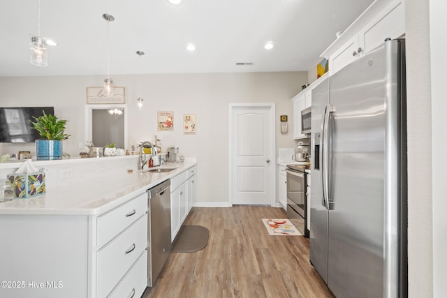 kitchen with appliances with stainless steel finishes, white cabinets, and decorative light fixtures