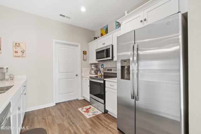 kitchen with appliances with stainless steel finishes, tasteful backsplash, sink, white cabinets, and light hardwood / wood-style flooring