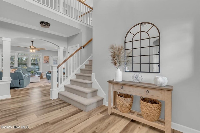 staircase featuring ceiling fan, wood-type flooring, decorative columns, and a high ceiling